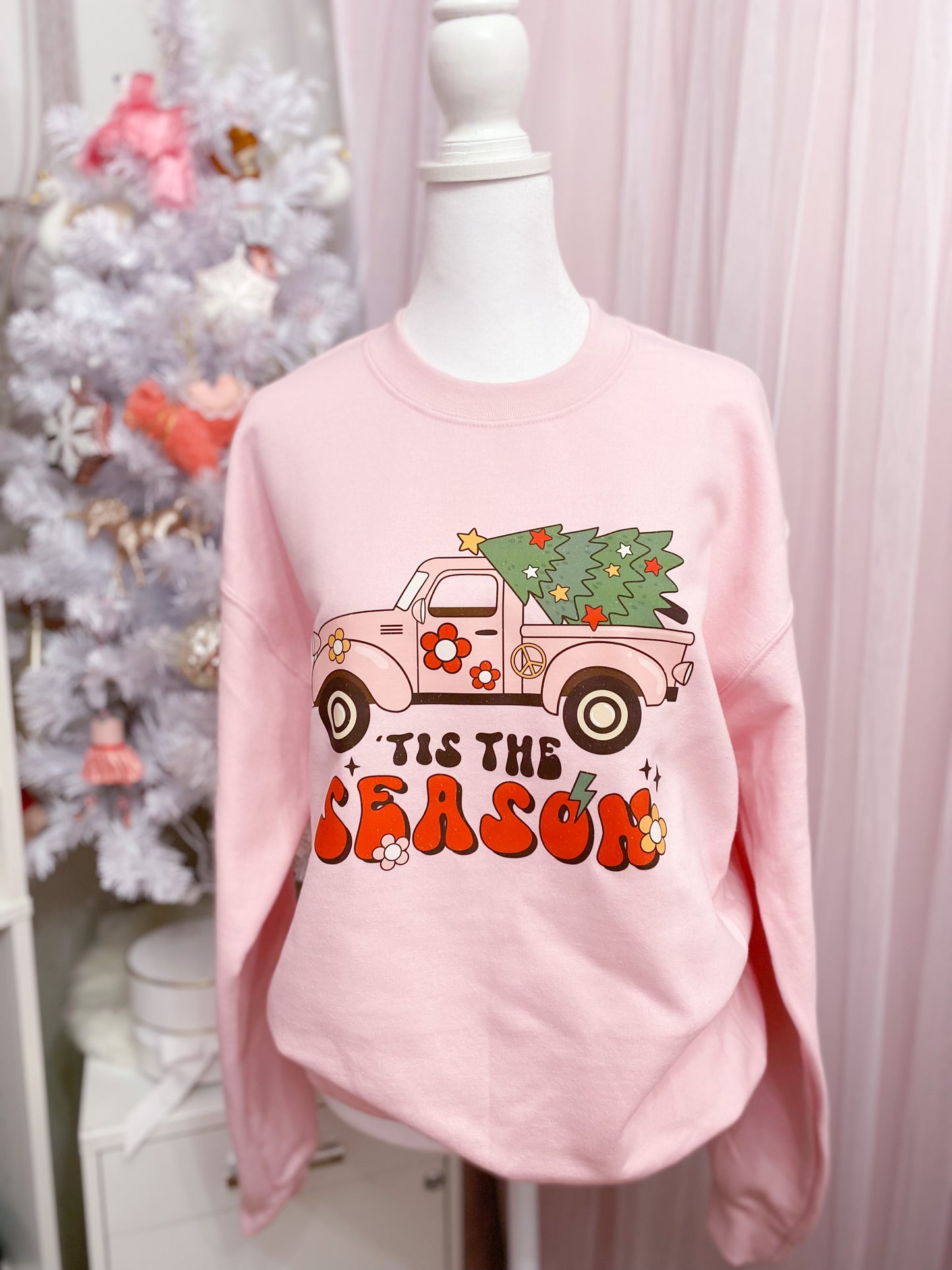 pink fleece crew neck sweatshirt with printed design saying 'TIS THE SEASON , including a pink truck carrying a Christmas tree